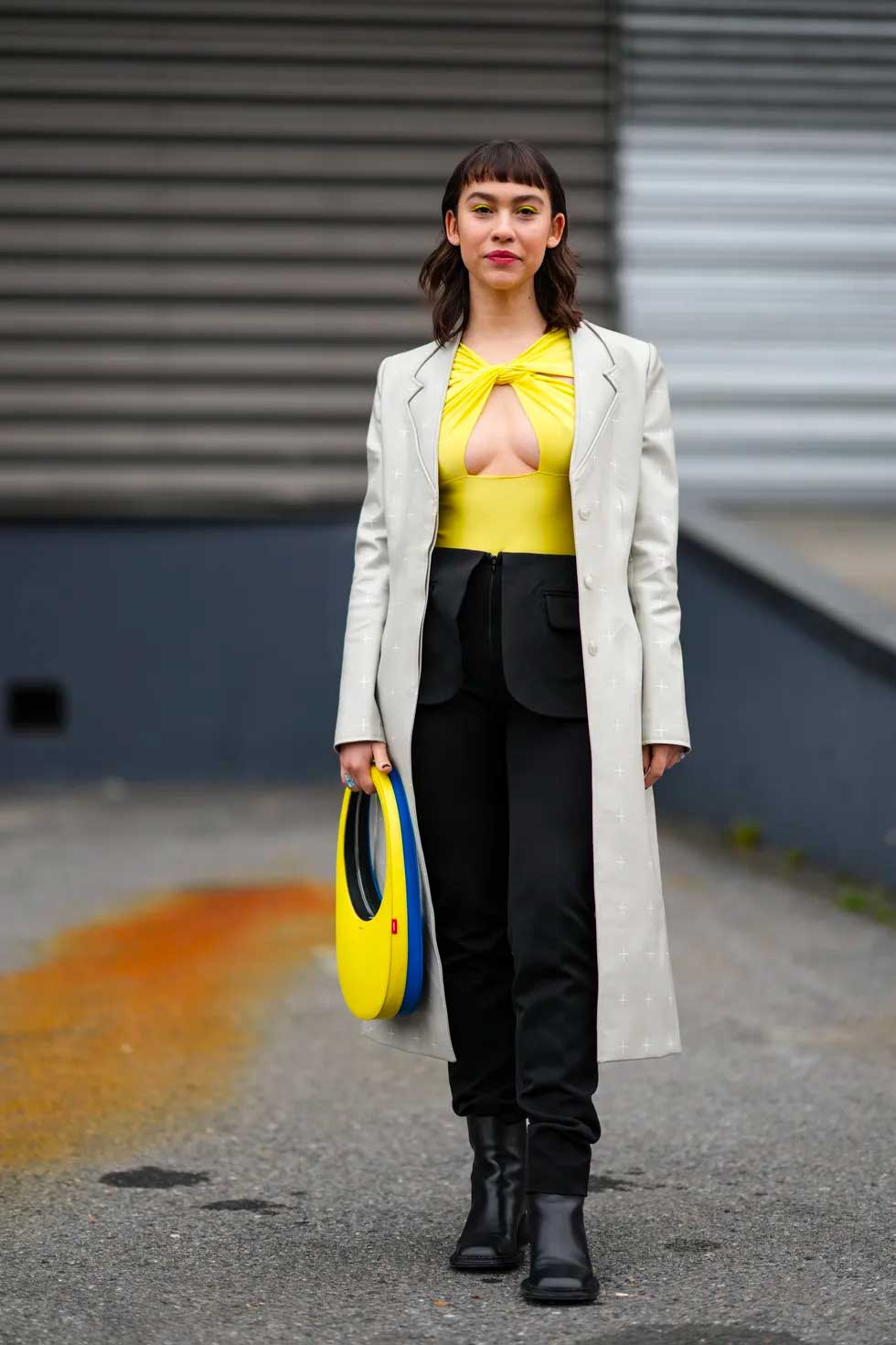 calça preta bolsa oval azul e amarela blusa amarela decote nos seios casaco bege