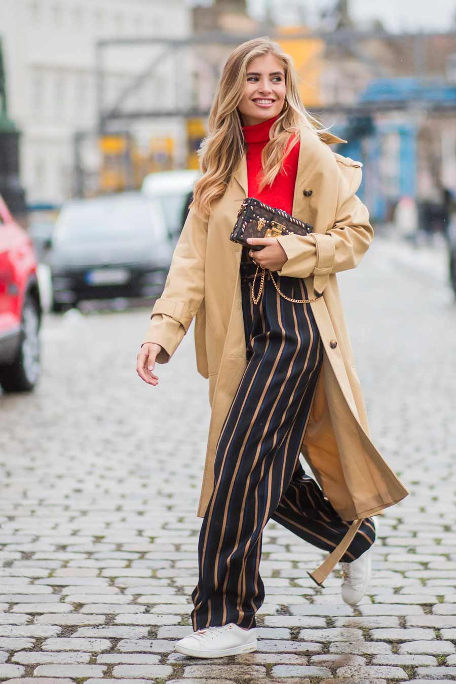 calça pantalona listrada preto e bege blusa gola alta vermelho trench coat bege tênis branco